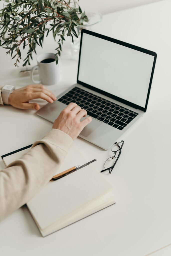 Professional working on a laptop with a notebook and glasses on a desk, symbolizing detailed contract and agreement review.